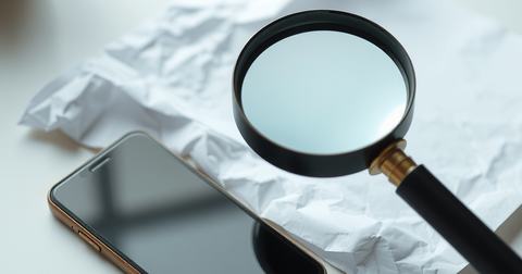 Vergrootglas boven een gekreukeld wit vel papier naast een smartphone